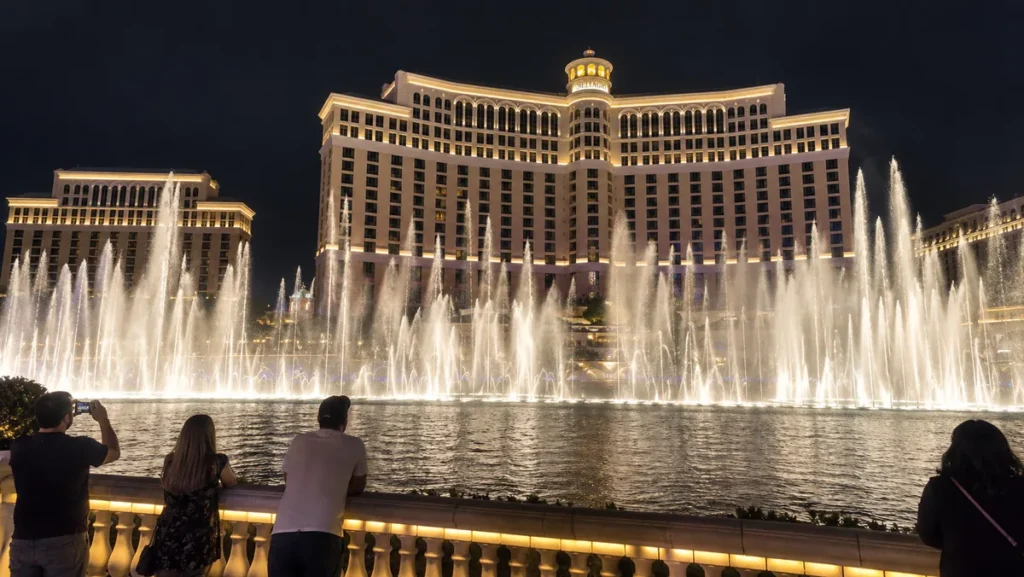 Bellagio Fountains performing in front of the illuminated Bellagio hotel at night.