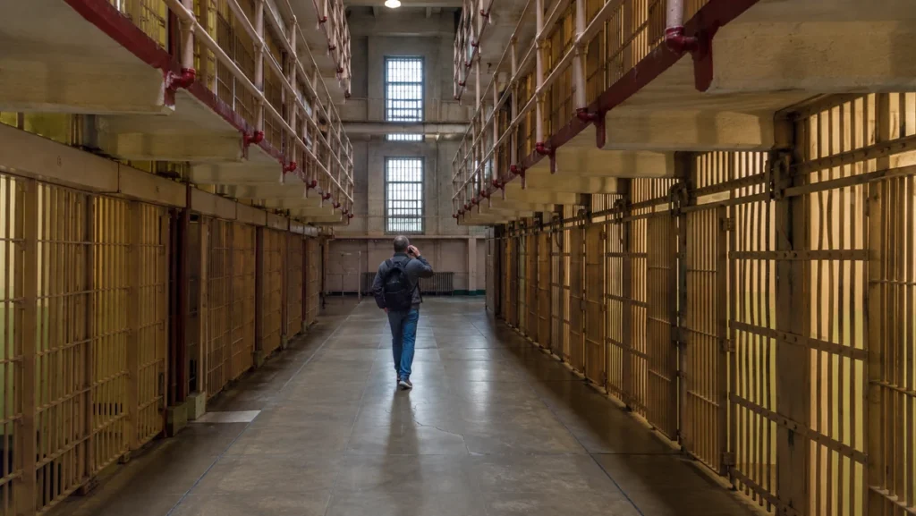 Historic Alcatraz cellblock corridor with a male visitor walking between rows of prison cells.